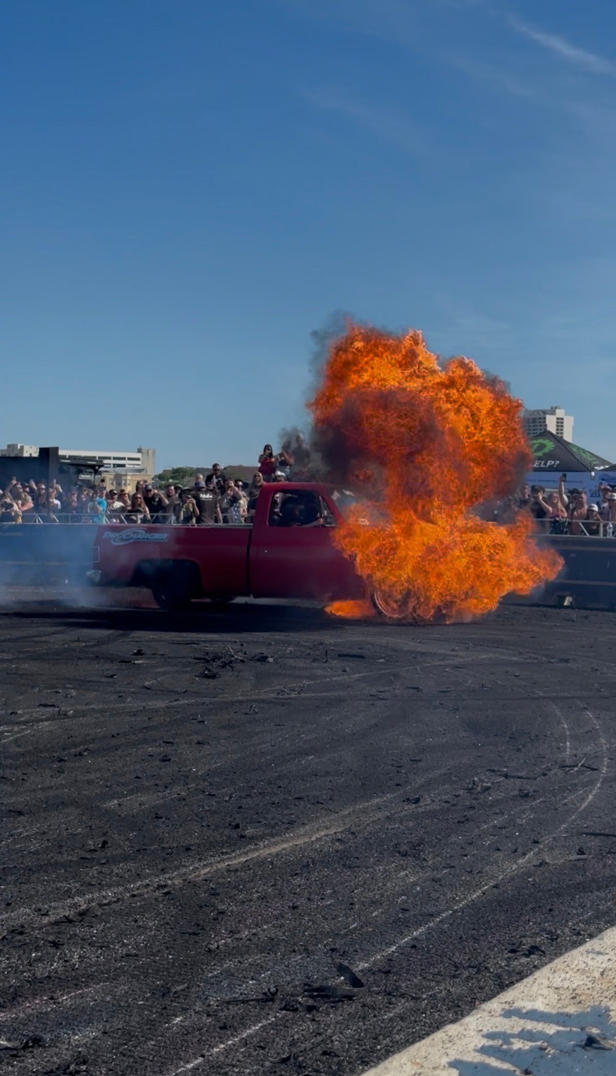 Red truck with its rear tire fully engulfed in flame at a burnout event